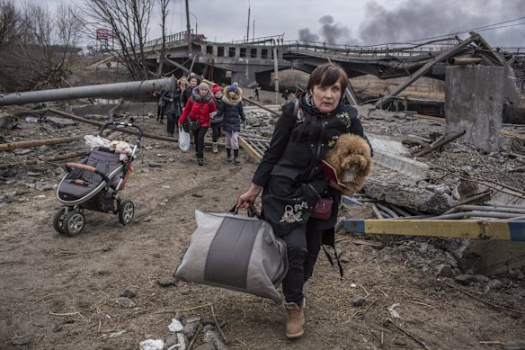 People cross an improvised path under a destroyed bridge while fleeing the town of Irpin.