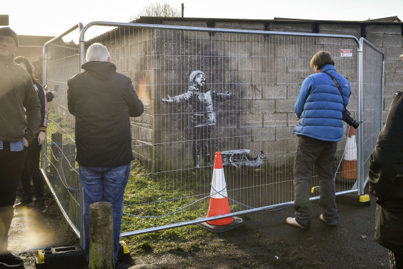 People take photographs through metal fencing, which has been erected to protect an artwork by street artist Banksy.