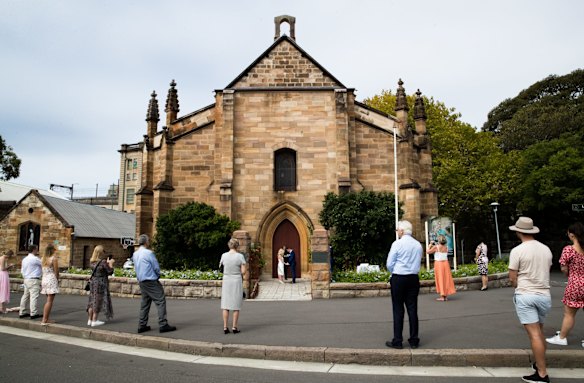 Passersby practice social distancing on the street while Brigette Leech and Matthew Selby are married by Minister Justin Moffatt, at the Garrison Church in Sydney. 