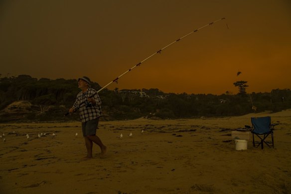 Pambula local Paulo fishing at Pambula Beach despite red skies and ash falling caused by bush fires.