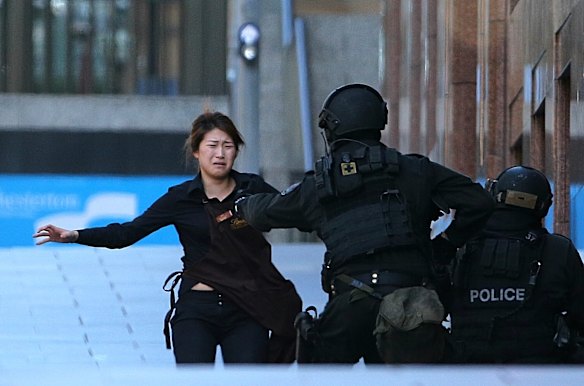 A hostage runs to armed tactical response police officers for safety after she escaped from Lindt cafe.
