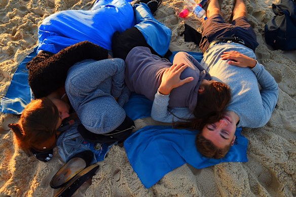 A group of people sleep as the sun rises over Bondi Beach.