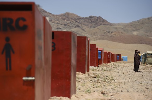 Passing a row of toilets, Ziba aged 21 years walks back to her family's temporary shelter in Regreshan IDP camp, carrying her son Suleiman aged 1 and a half years old who is suffering from severe acute malnutrition (SAM).
