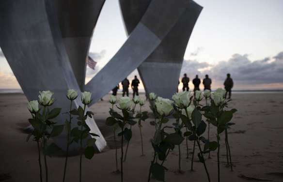 Men in a vintage US WWII uniforms stand behind flowers left at Les Braves monument after a D-Day 76th anniversary ceremony in Saint Laurent sur Mer, Normandy, France, Saturday, June 6, 2020. Due to coronavirus measures many ceremonies and memorials have been cancelled in the region with the exception of very small gatherings. 