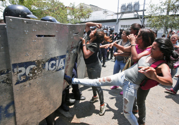 A woman kicks at a riot police shield as relatives of prisoners wait to hear news about their family members imprisoned at a police station where a riot broke out, in Valencia, Venezuela.