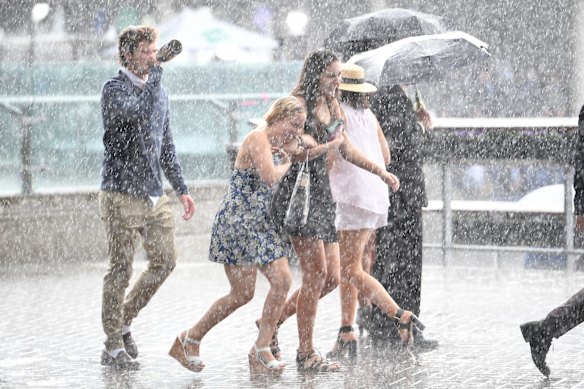 Racegoers are seen walking through heavy rain during The TAB Everest race day at Royal Randwick Racecourse.