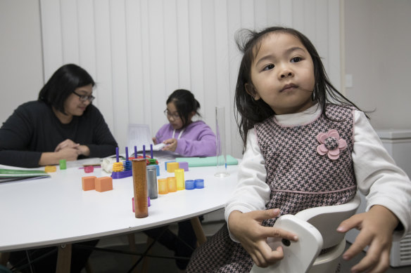 Kam Wong sits at the family dinning room table and helps her nine-year-old daughter Katrina with her maths homework, while three-year-old Kinsey counts blocks.