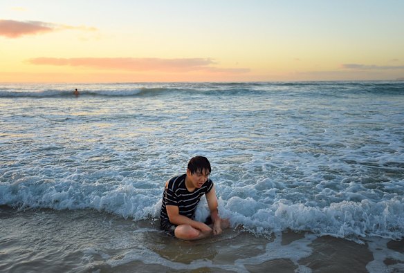 A man visiting from Korea sits exhausted in the water as the sun rises over Bondi Beach.