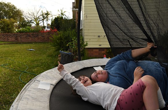 Maria Moschetti and her daughter Lily Thomson, who has autism,  look at clouds whilst lying on a trampoline in the front yard of their home in Fairfield. Sometimes neighbours drop surprise bags of lollies at Lily’s gate, and the family pays it forward: Ms Moschetti delivers hampers with groceries to doorsteps on her street and her partner mows lawns of the elderly. They’ve also made cupcakes to deliver to the local police station and hospital.
