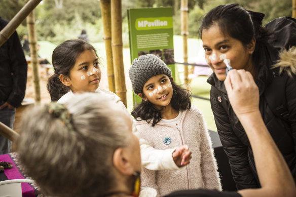 Adele and Alyssa watch their mum Lysander get her face painted in traditional Indigenous style by Merilyn Duff at Melbourne Zoo to open NAIDOC Week on July 2.