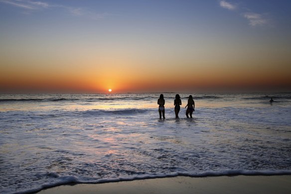 Three women dip the legs in at Coogee as the Sun peeks over the horizon.