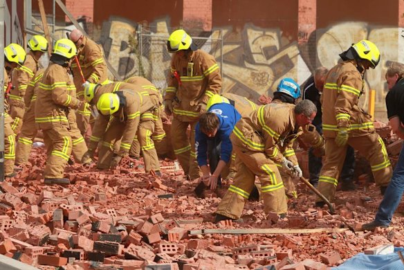 Firemen and workers with bare hands frantically remove bricks.