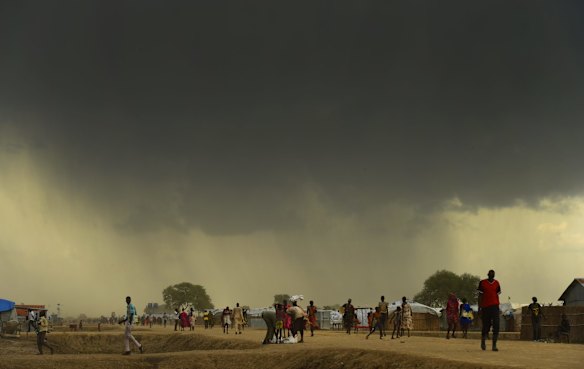 People walk along a road as the rains come inside UN Bentiu Protection of Civilians (POC) site, home to over 100,000 people who have fled violence and food insecurity. Bentiu, Unity State, South Sudan.