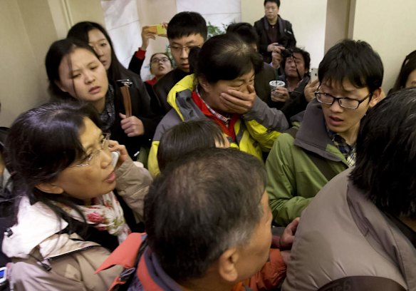 A woman, center, surrounded by media covers her mouth on her arrival at a hotel which is prepared for relatives or friends of passengers aboard a missing airline, in Beijing, China.