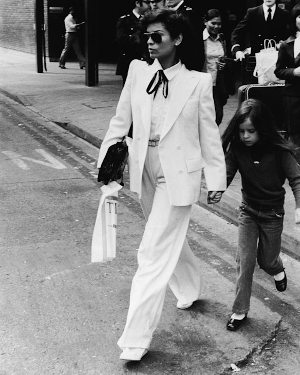 Nicaraguan-born model Bianca Jagger wears a double-brested white suit as she and her daughter Jade walk across the street in front of a group of policemen in London, May 4, 1979. (Photo by Express Newspapers/Getty Images)