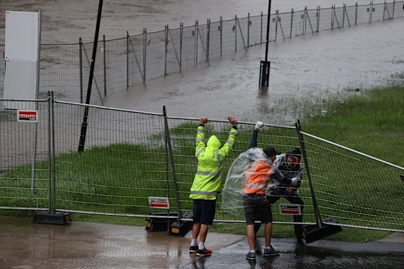 Men struggle to lift a fallen fence that surrounds the Powerhouse Museum site with the rising Parramatta River.