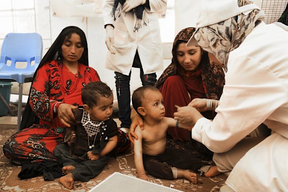 Ziba aged 21 years (2nd from right) holds her son Suleiman aged 1 and a half years old whilst he is tested for severe acute malnutrition (SAM) by medical staff in a nutrition centre in Regreshan IDP camp in Herat Province.
