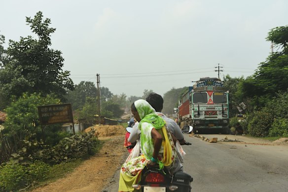 A man and woman ride their motorbike towards a broken-down coal truck on the road from the PEKB coal mine, in Chhattisgarh province, central India. Villagers around the mine, which is operated by Adani Mining, claim that the trucks have ruined the roads and polluted the countryside.