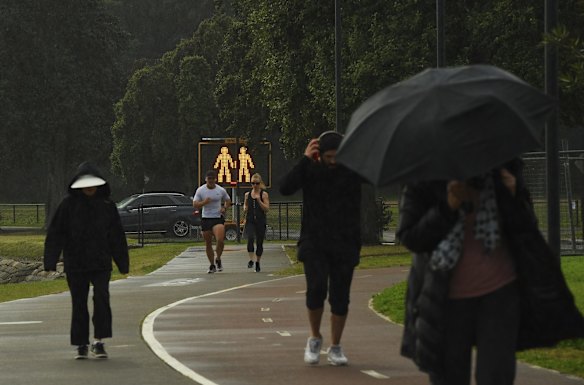 People pass a sign reminding them to social distance along a track past on the Bay Run on day two of the Sydney lockdown in Lilyfield.