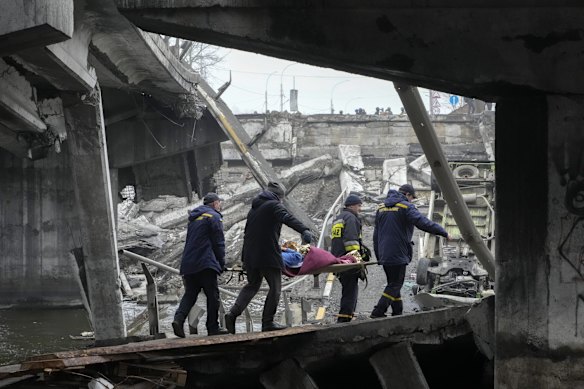 Rescue workers carry an elderly woman under a destroyed bridge in Irpin, close to Kyiv.