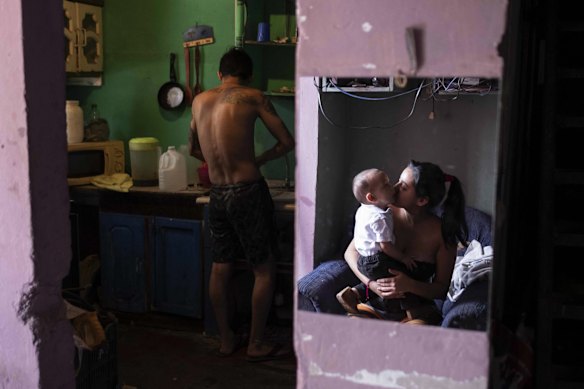 A man (L), unemployed due to the coronavirus crisis, does housework as a woman reflected in a mirror (R) kisses a child, in San Jose, Costa Rica. 