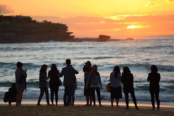 People gather at the shoreline as the sun rises over Bondi Beach.