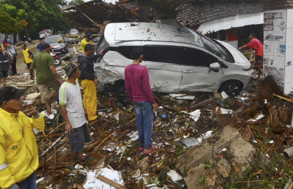 People inspect the wreckage of a car swept away by a tsunami.
