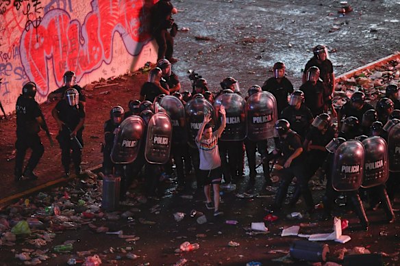 A man walks by police clashing with soccer fans who waited for hours for a homecoming parade for the players who won the World Cup at the Obelisk in Buenos Aires, Argentina. A parade to celebrate the champions was abruptly cut short Tuesday as millions of people poured onto thoroughfares, highways and overpasses in a chaotic attempt to catch a glimpse of the national team.