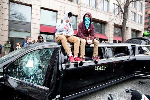 Demonstrators sit at the top of a limousine with the windows broken during the demonstration in downtown Washington.