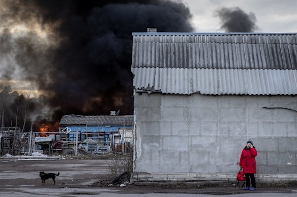 A woman shelters behind a building as smoke and flames rise from a chemical warehouse that was hit by Russian shelling on the eastern front-line near Kalynivka village in Kyiv, Ukraine. 