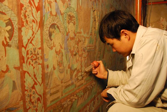 A conservator works to preserve a deteriorated mural in the Mogao Caves. Photo: Conrad Walters.