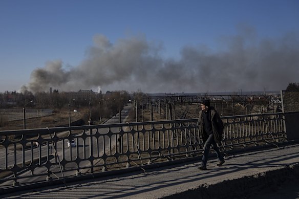 A pedestrian looks at a cloud of smoke rising after an explosion in Lviv, western Ukraine. The mayor of Lviv says missiles struck near the city's airport early Friday.