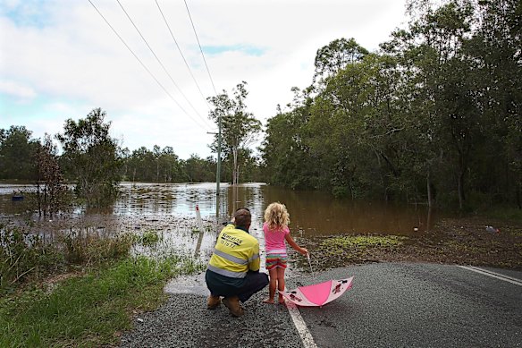 Adam Nelson and daughter Chloe Nelson, 5, look out at flood water near their home outside Jimboomba.