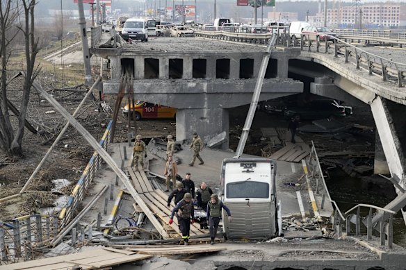 Ukrainian soldiers carry a body of a civilian killed by the Russian forces over the destroyed bridge in Irpin close to Kyiv.