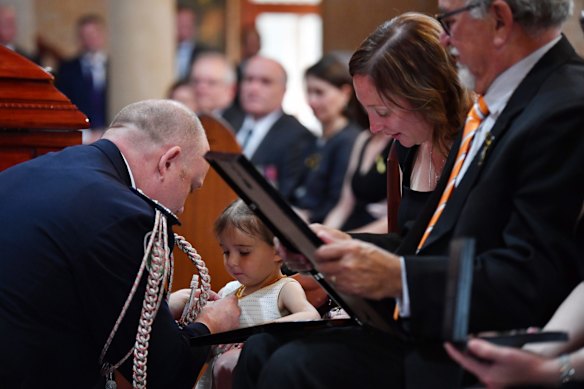 Charlotte O'Dwyer, the young daughter of Rural Fire Service volunteer Andrew O'Dwyer, with Andrew's wife Melissa receives her fathers service medal from RFS Commissioner Shane Fitzsimmons.