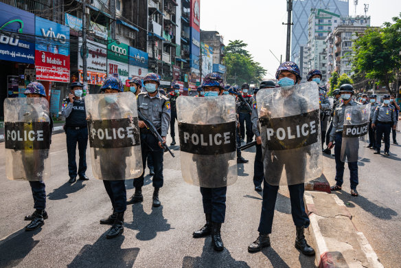 Riot police stand guard as anti-coup protesters march through the streets.