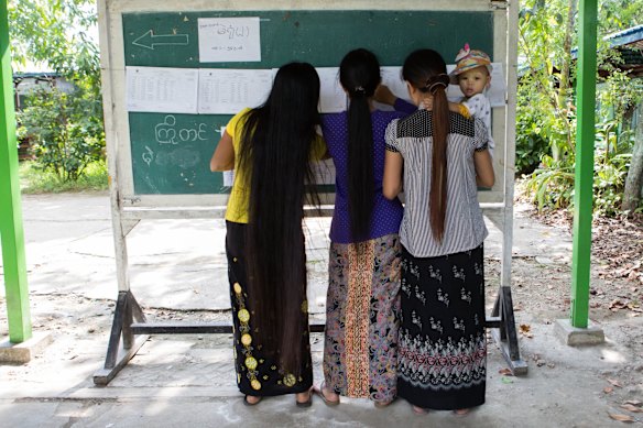 Women search for names on a voter's registration list at a polling station in the village of Dala, Myanmar.