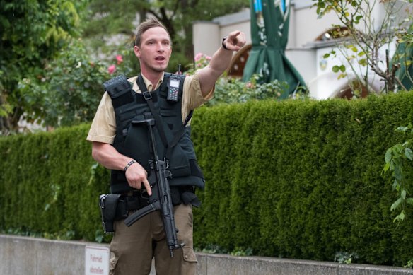 A heavily armed police officer points something out outside the Olympia mall.