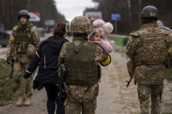 A Ukrainian soldier carries a baby helping a fleeing family to cross the Irpin river in the outskirts of Kyiv.