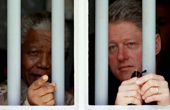 President Bill Clinton and Mandela peer through the bars of the cell in which Mandela spent 17 years while incarcerated by the former South African government. 1998.