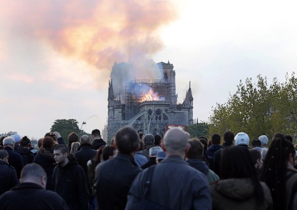 People watch as flames and smoke rise from Notre Dame cathedral.