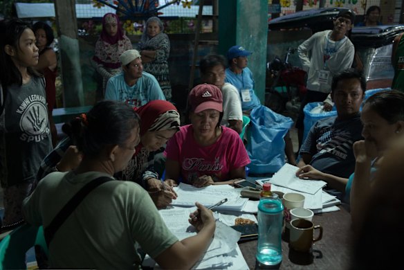 Local government workers call out the names of evacuees to distribute relief goods .