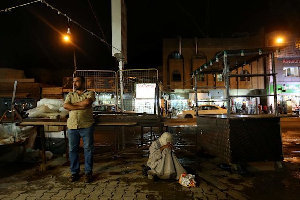 A man stands as another sits on the ground selling chewing gum on the location of a recent bombing on Karada street in Karada area in Baghdad.