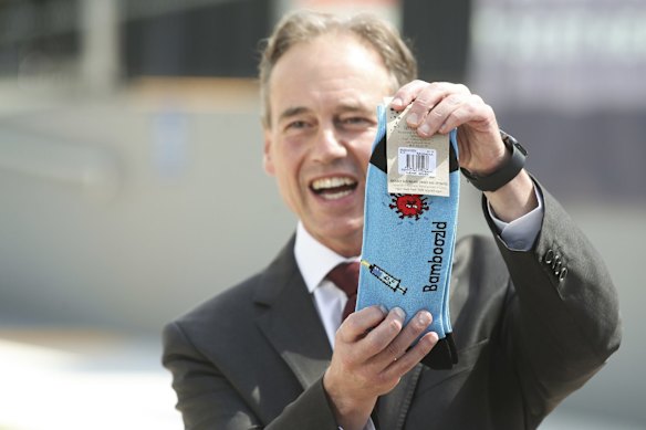 Health Minister Greg Hunt holds up a pair of COVID-19 vaccination-themed socks given to him by Dr Nick Coatsworth.