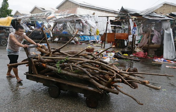 A resident pushes a cart full of wood as he passes market stalls destroyed by strong winds.