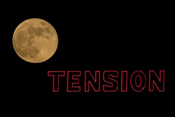 The full moon rises beyond a sign on top of a building in Kansas City.