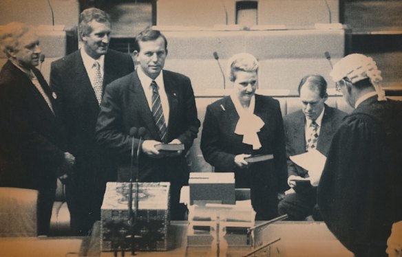 House of Representatives 1994. Former Liberal Party leader Andrew Peacock (far left), present leader Dr John Hewson (2nd left), new member and touted as a future leader Tony Abbott (3rd left), Bronwyn Bishop being sworn in by Reps Clerk, Govt Minister Gary Johns (seated right)