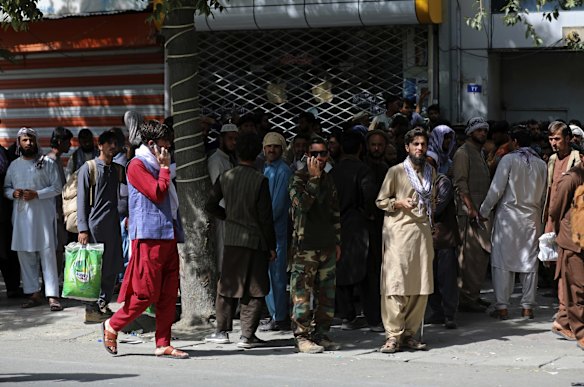 Afghans wait in long lines for hours to withdraw money, near Kabul Bank, in Kabul, Afghanistan.. Officials say Taliban fighters have entered Kabul and are seeking the unconditional surrender of the central government. 
