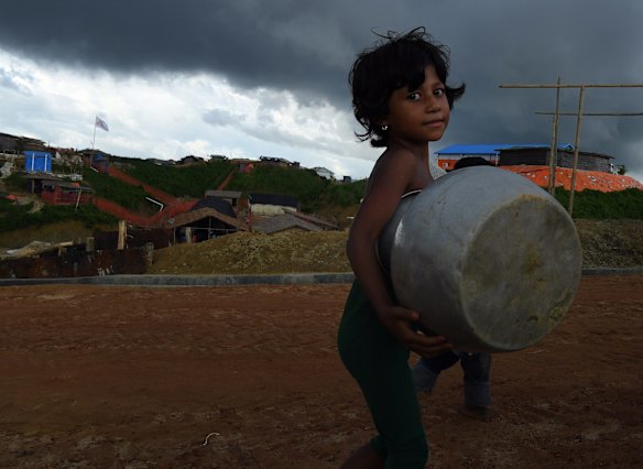 Storm clouds hang overhead as a child carries a pot whilst walking on a main road in Kutupalong camp. Kutupalong & Balukhali camps, combined is the largest refugee camp in the world, home to over 400,000 of 900,000 Rohingya refugees who fled Myanmar in August 2017.