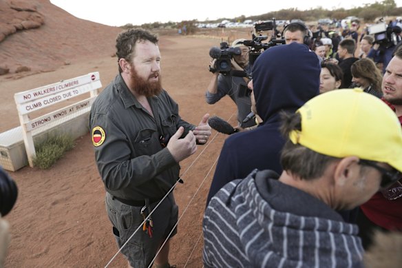 A ranger tells people the climb is on hold due to strong winds, on the final day the climb is allowed, at Uluru.
